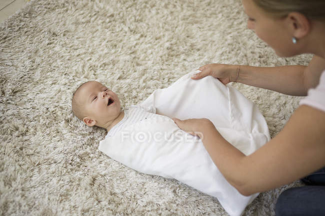 Пеленание шаг 5. Мать заворачивает и укладывает малыша одеялом — стоковое фото