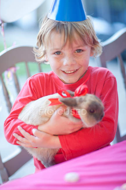 Jeune garçon anniversaire étreignant son lapin — Photo de stock