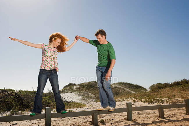 A young man helping a woman balancing on a fence — Stock Photo