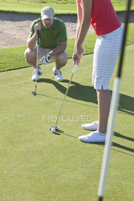 Jovem do sexo feminino alinhando bola de golfe com treinador — Fotografia de Stock