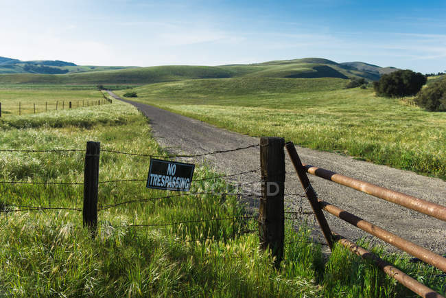 Dirt track between green fields and no trespass sign — Stock Photo