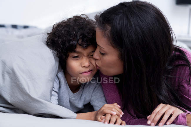Mãe beijando filho na bochecha na cama — Fotografia de Stock