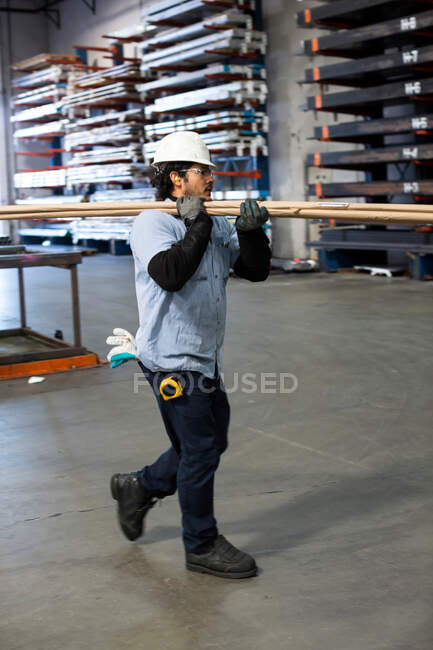 Worker carrying pipes in metal plant — Stock Photo