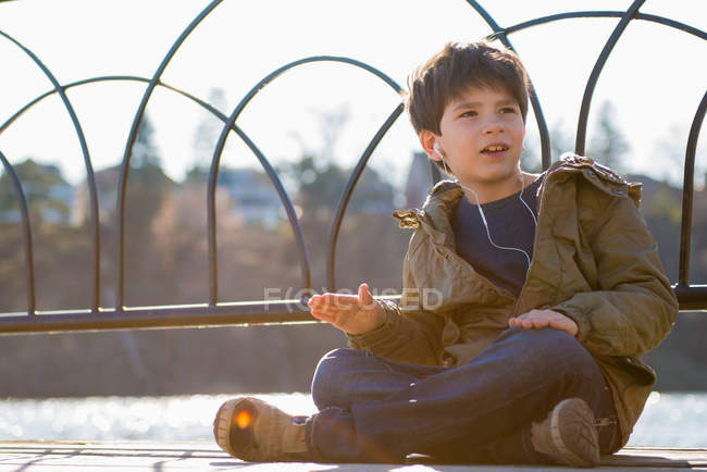 Niño sentado con las piernas cruzadas usando auriculares - foto de stock
