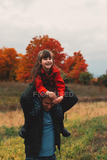 Средний взрослый мужчина дает дочери плечо носить в поле — стоковое фото