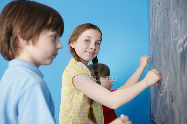Kinder schreiben auf Tafel, blauer Hintergrund — Stockfoto