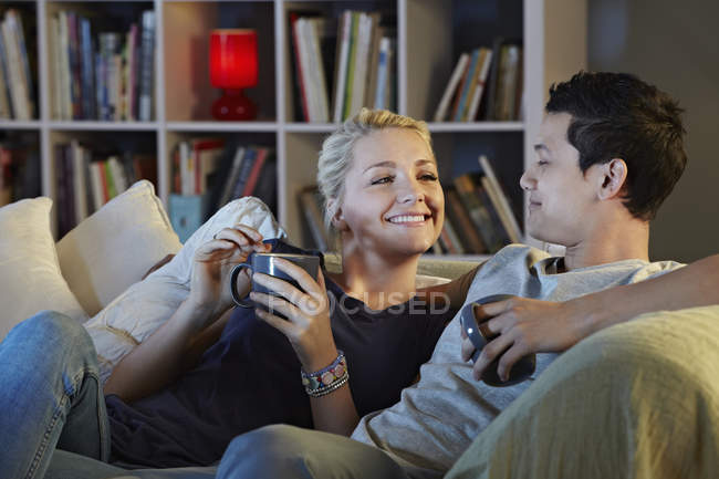 Молода пара сидить на дивані з гарячими напоями — стокове фото