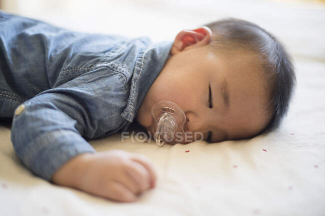 Baby boy with pacifier sleeping on bed — Stock Photo