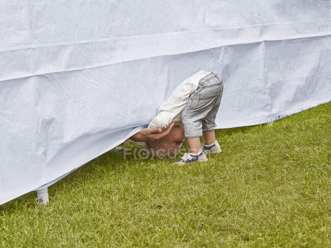 Giovane ragazzo piegandosi in avanti per raggiungere padri mano sotto tenda — Foto stock