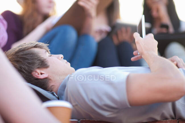 Молодой человек лежит с помощью смартфона — стоковое фото