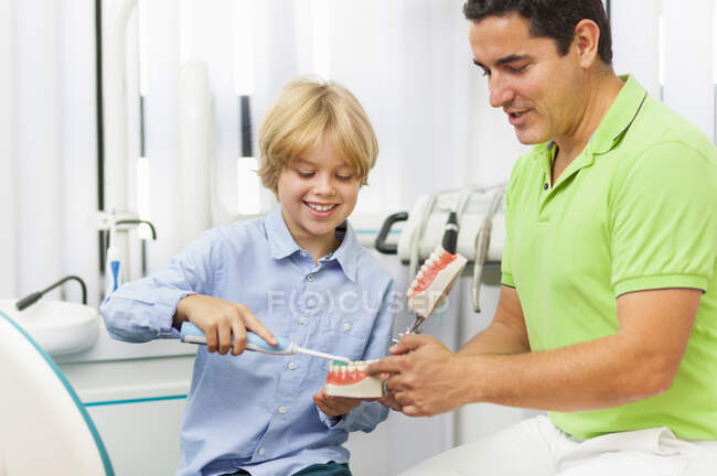 Дантист учит мальчика чистить зубы — стоковое фото