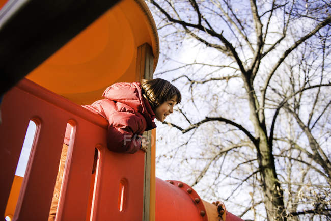 Garoto olhando para fora do topo da corrediça do playground vermelho — Fotografia de Stock