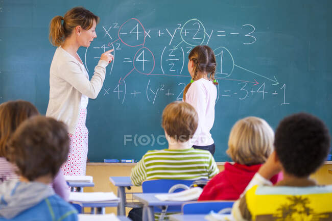 Primary school teacher explaining equation on classroom blackboard — Stock Photo