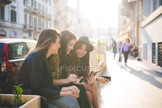 Three young women using digital tablet on city street — Stock Photo