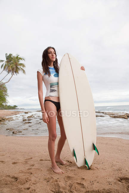 Молодая женщина держит доску для серфинга на пляже — стоковое фото