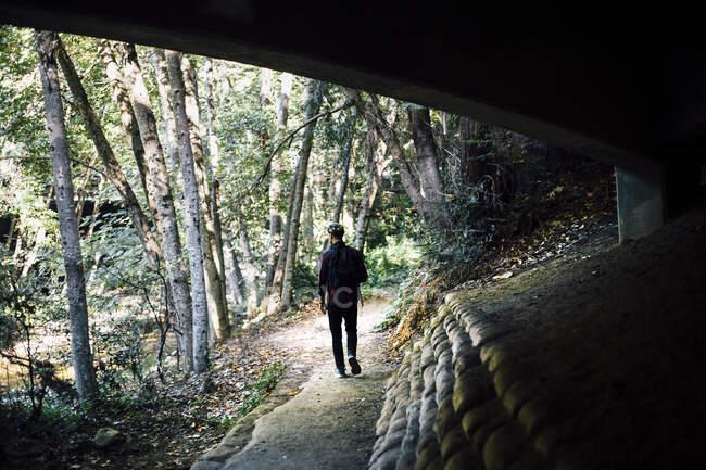 Um homem com um casaco preto e uma mochila caminha ao longo do caminho na floresta — Fotografia de Stock