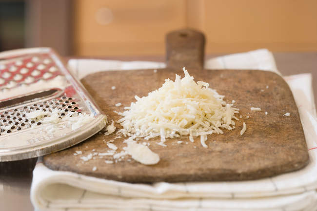 Grated cheese and grater on wooden board — Stock Photo
