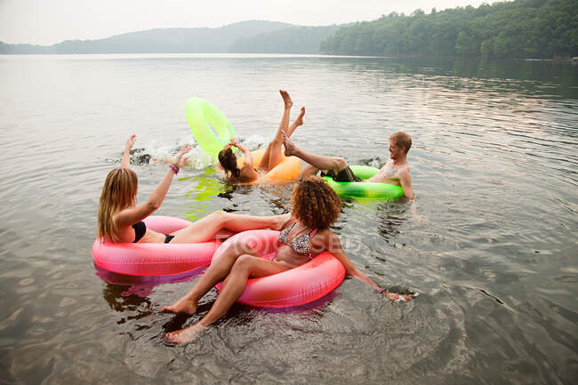 Друзья играют в надувных кольцах на озере — стоковое фото