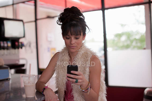 Молодая женщина смотрит на мобильный телефон в закусочной — стоковое фото