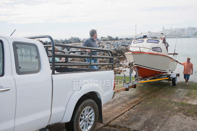 Jeunes hommes avec bateau à moteur et remorque dans le port — Photo de stock