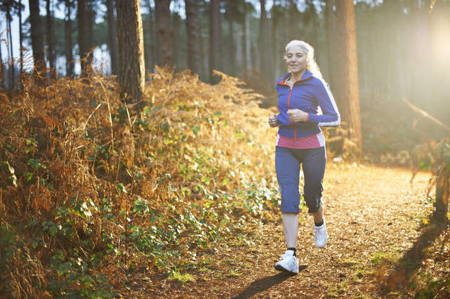 Reife Frau joggt auf Waldweg — Stockfoto