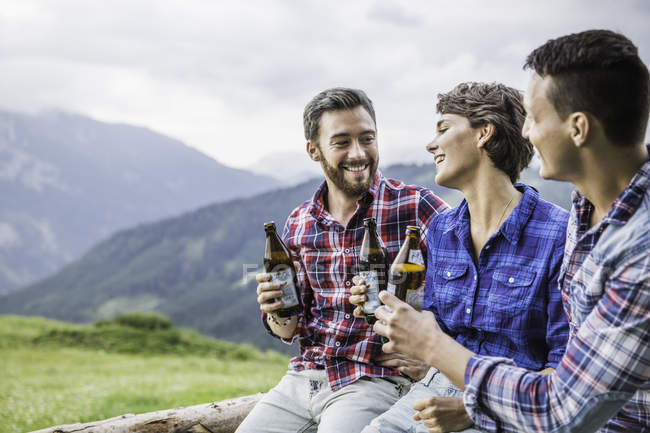 Tres jóvenes amigos bebiendo cerveza en la valla - foto de stock