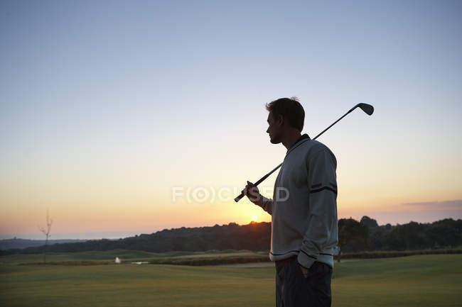 Golfista carregando taco de golfe sobre ombro olhando para o pôr do sol — Fotografia de Stock