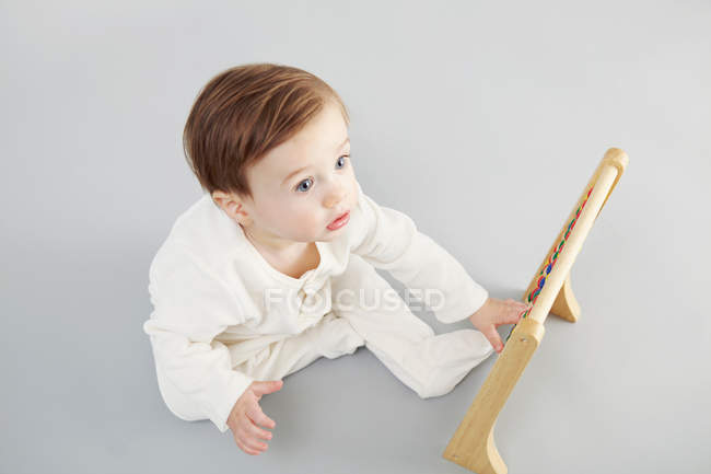 Baby boy looking at abacus while sitting on floor — Stock Photo