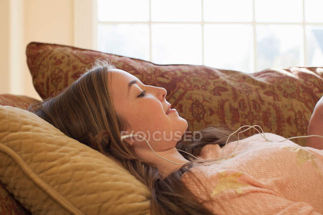 Adolescente couchée sur un canapé avec des écouteurs — Photo de stock
