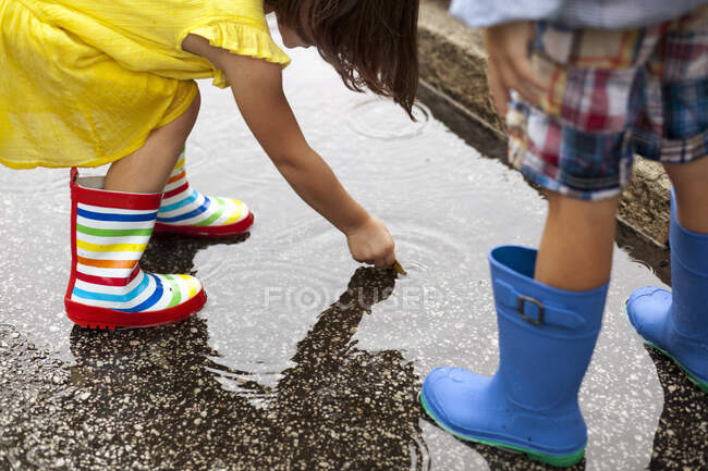 Ragazzo e sorella indossando stivali di gomma guardando giù in pozzanghera pioggia — Foto stock