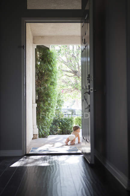 Rückansicht eines Jungen mit Windel, der durch offene Haustür kriecht — Stockfoto
