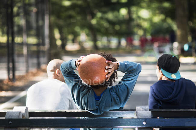 Jóvenes sentados en el parque, uno sosteniendo baloncesto - foto de stock