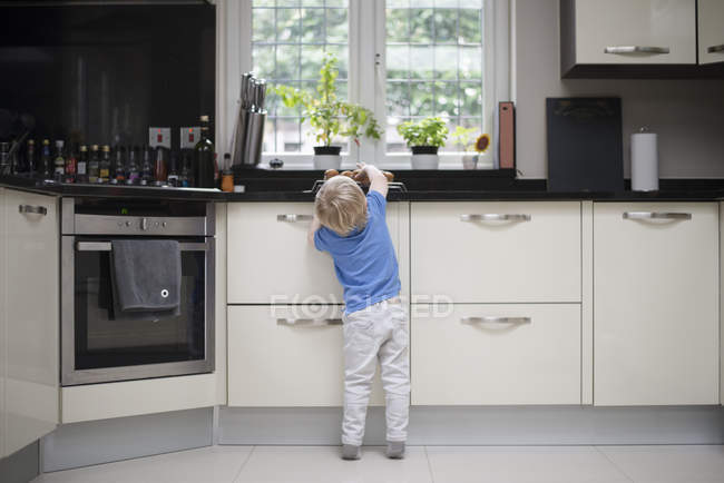 Jeune garçon dans la cuisine, levant la main pour des muffins, vue arrière — Photo de stock