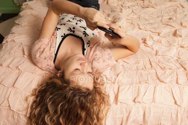 Дівчина-підліток лежить на ліжку зі смартфоном — стокове фото