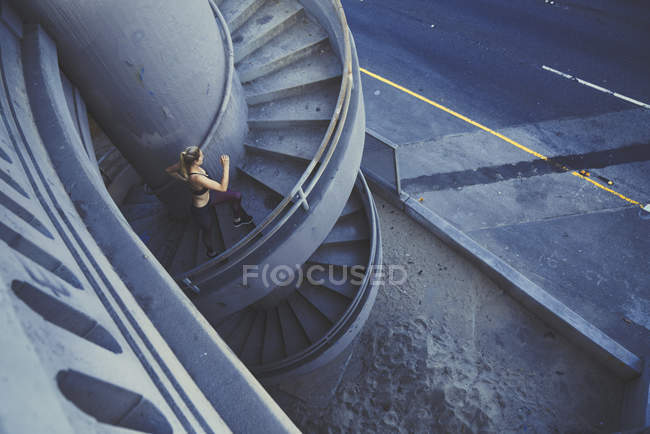 Young woman running up spiral staircase outdoors — Stock Photo
