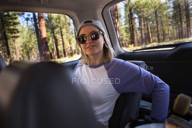 Retrato de mulher jovem usando óculos de sol em banco traseiro do carro — Fotografia de Stock