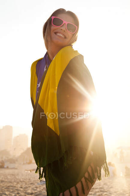 Mujer joven envuelta en bandera brasileña a la luz del sol - foto de stock