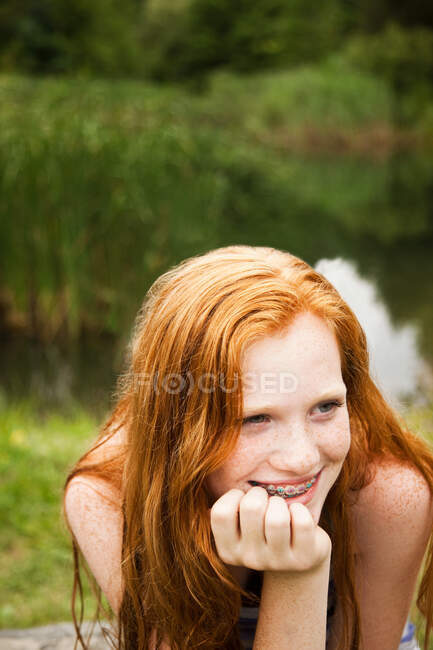 Ragazza adolescente sorridente agli amici con un lago dietro di lei — Foto stock
