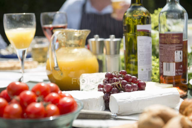 Grapes, tomatoes and cheese with drinks at table — Stock Photo