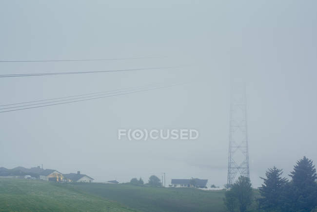 Misty view of electricity cables and pylon next to houses — Stock Photo