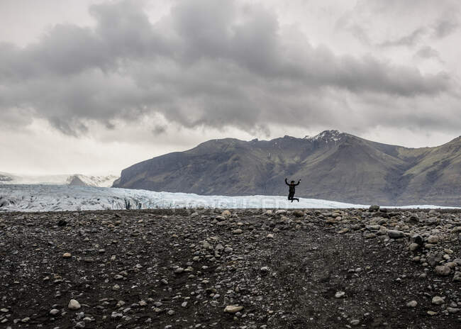 Silueta de turista femenina saltando en el aire frente al glaciar, Skaftafell, Islandia - foto de stock