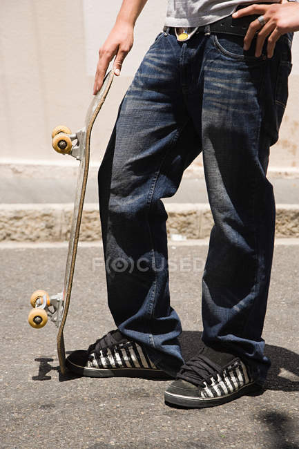 Cropped image of teenage skateboarder standing on street with longboard — Stock Photo