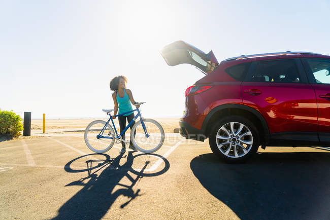 Mujer adulta media poniendo bicicleta en el maletero del coche - foto de stock
