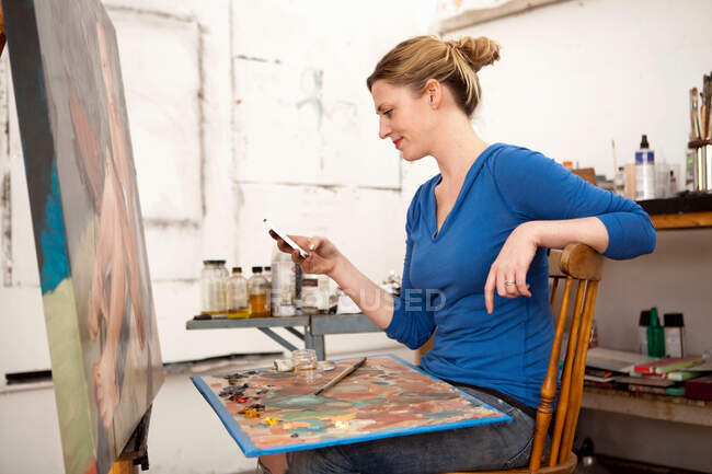 Жінка середнього віку, що використовує мобільний телефон у студії художника — стокове фото