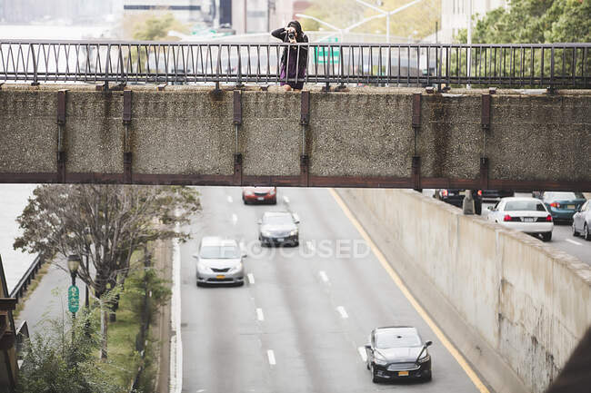 Молода жінка стоїть на пішохідному мосту, фотографує — стокове фото