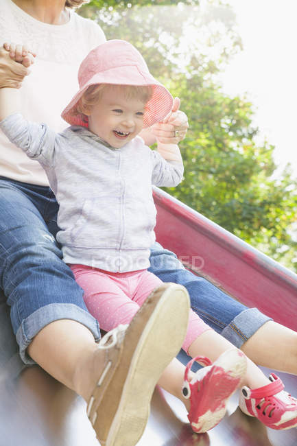 Madre e femmina bambino scorrevole sullo scivolo del parco — Foto stock