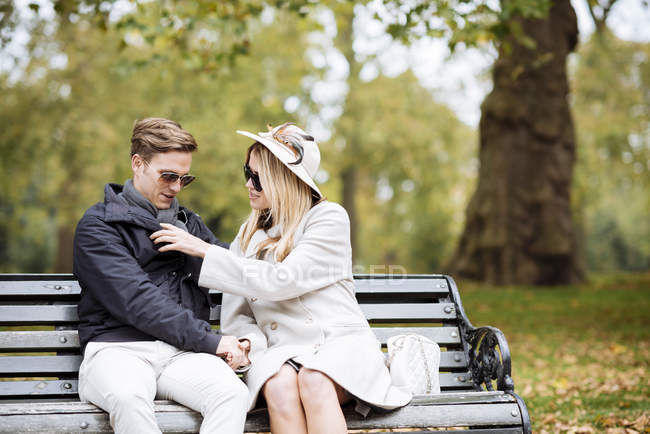 Elegante pareja joven sentada en el banco del parque - foto de stock