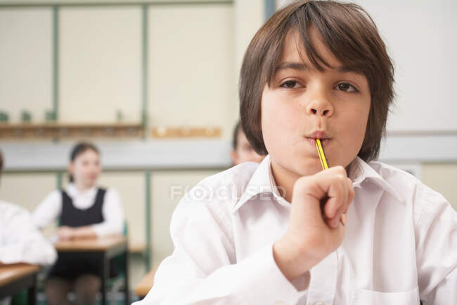Menino com lápis na boca, na sala de aula — Fotografia de Stock