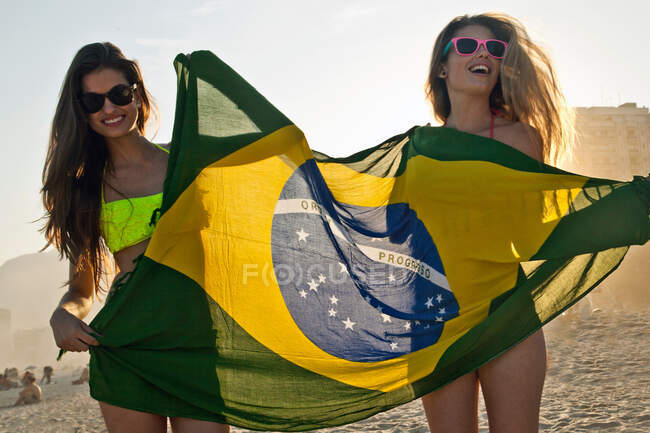 Duas jovens mulheres se divertindo na praia com bandeira brasileira — Fotografia de Stock