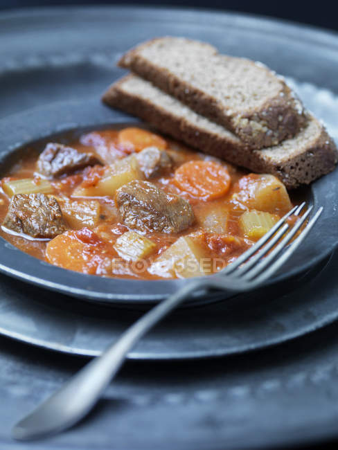 Plate of navarin of lamb with carrots, celery, tomatoes and wholegrain bread — Stock Photo